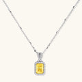 Rectangular yellow moissanite pendant in sterling silver halo setting on delicate chain against cream background.