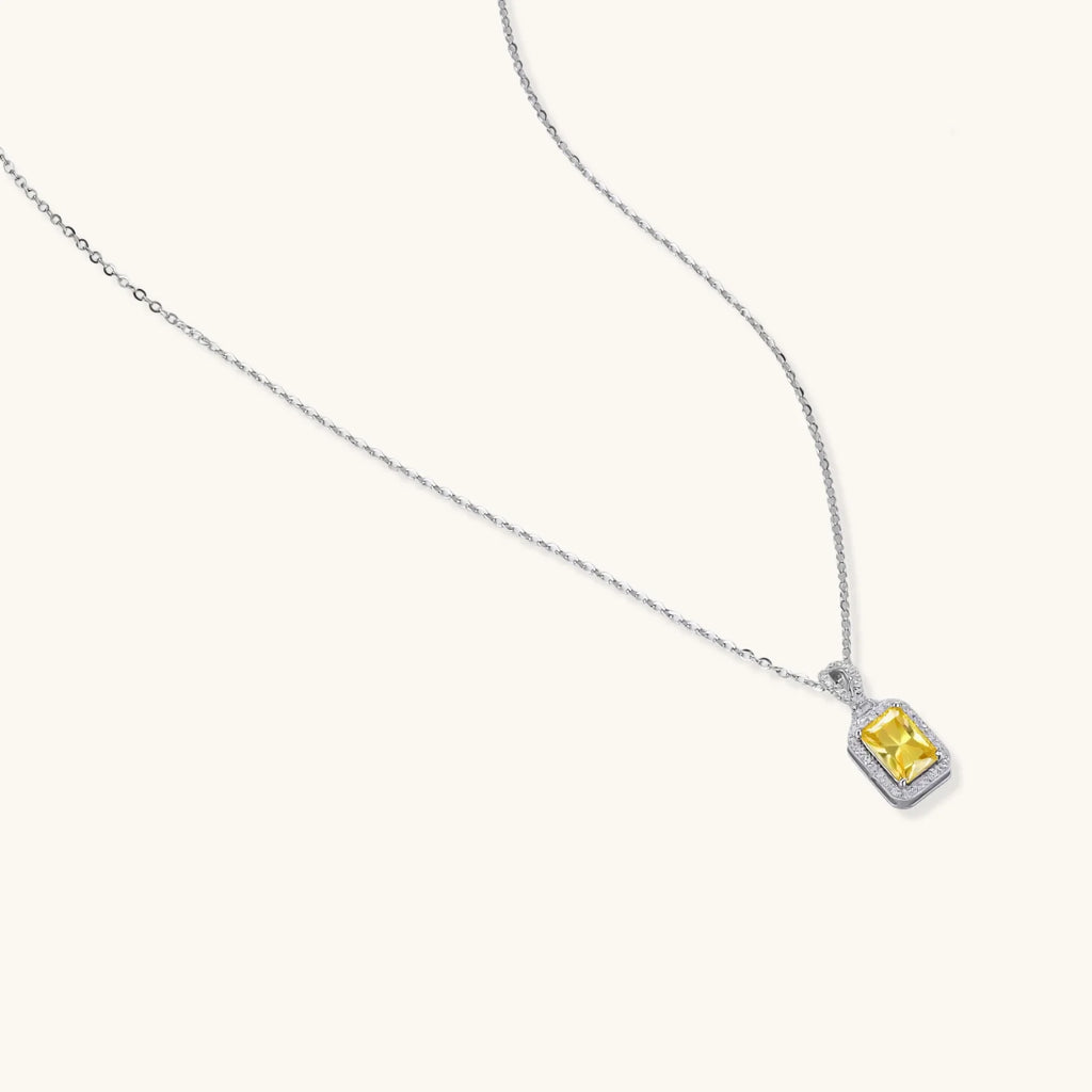 Rectangular yellow moissanite pendant in sterling silver halo setting on delicate chain against cream background.