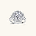 Brilliant round moissanite center stone with baguette and round halo accents in sterling silver setting on light background.
