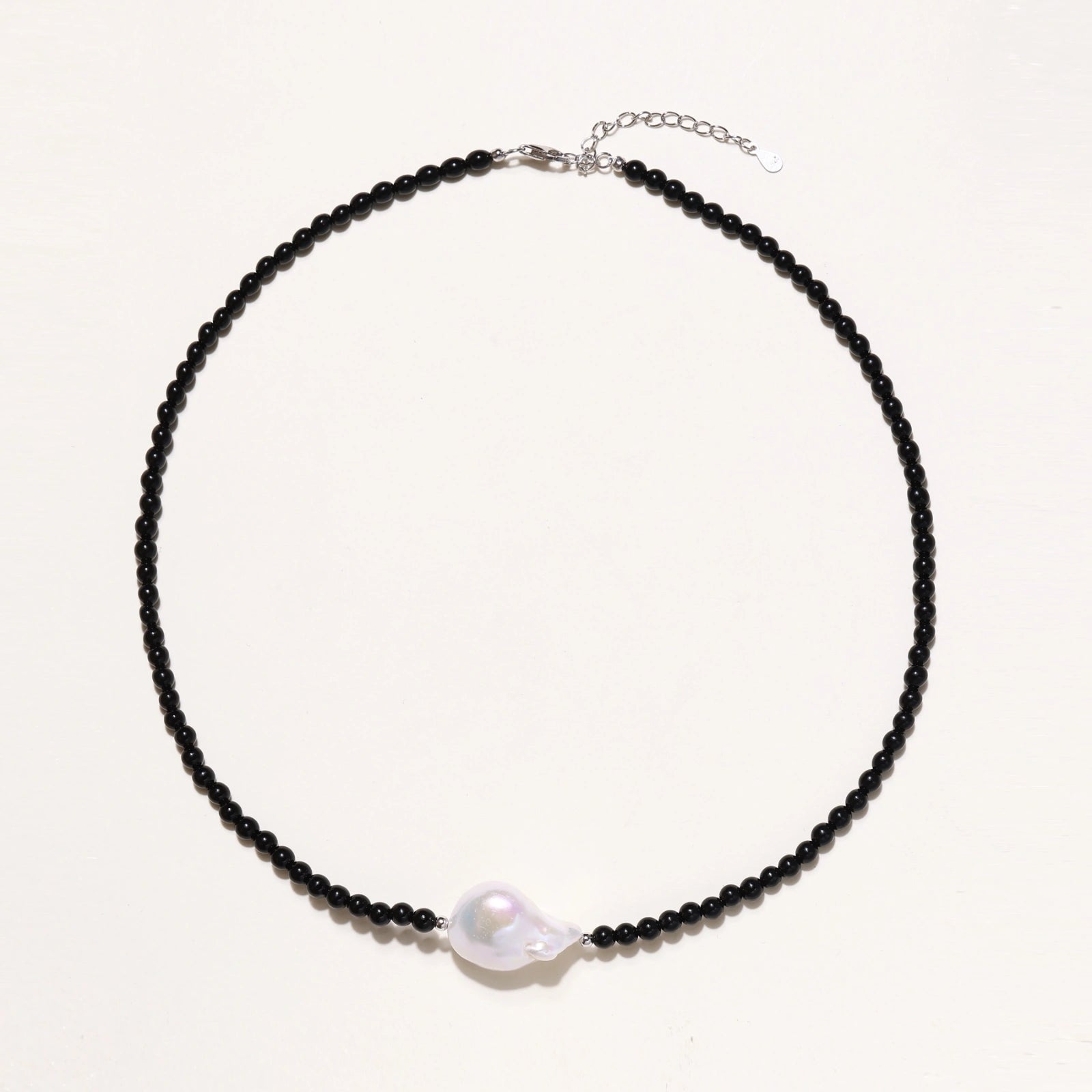 Beaded black agate necklace with iridescent baroque freshwater pearl centerpiece on cream background.